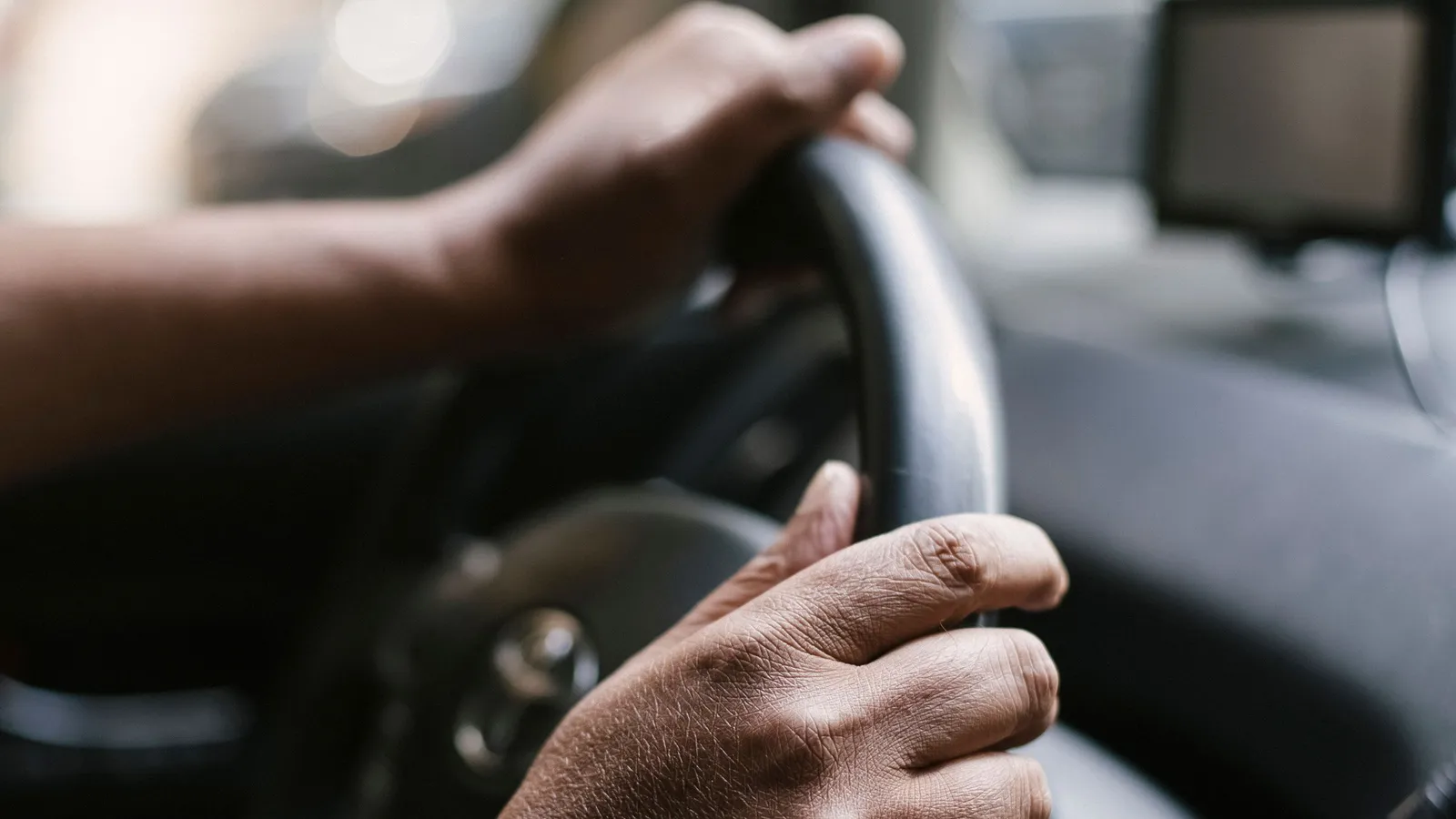 Mãos de um motorista ao volante de um carro, com o suporte do telemóvel desfocado ao fundo